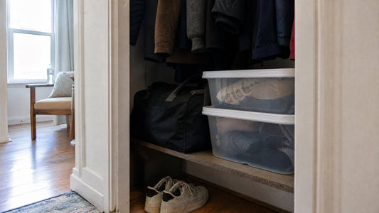 A plain dark duffel bag and two clear storage bins on a low shelf in an apartment entryway closet