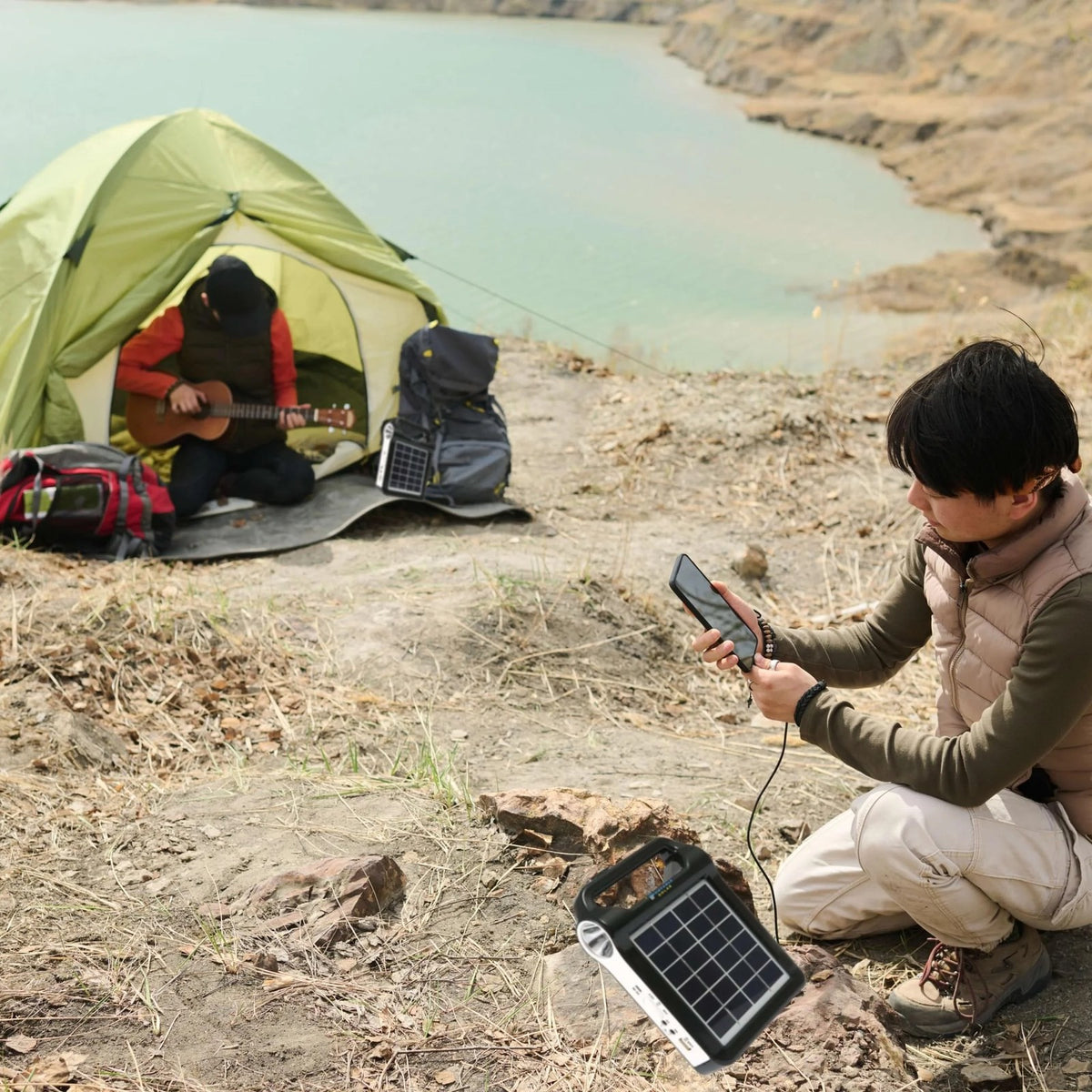 Portable solar power station charging a phone at a lakeside campsite