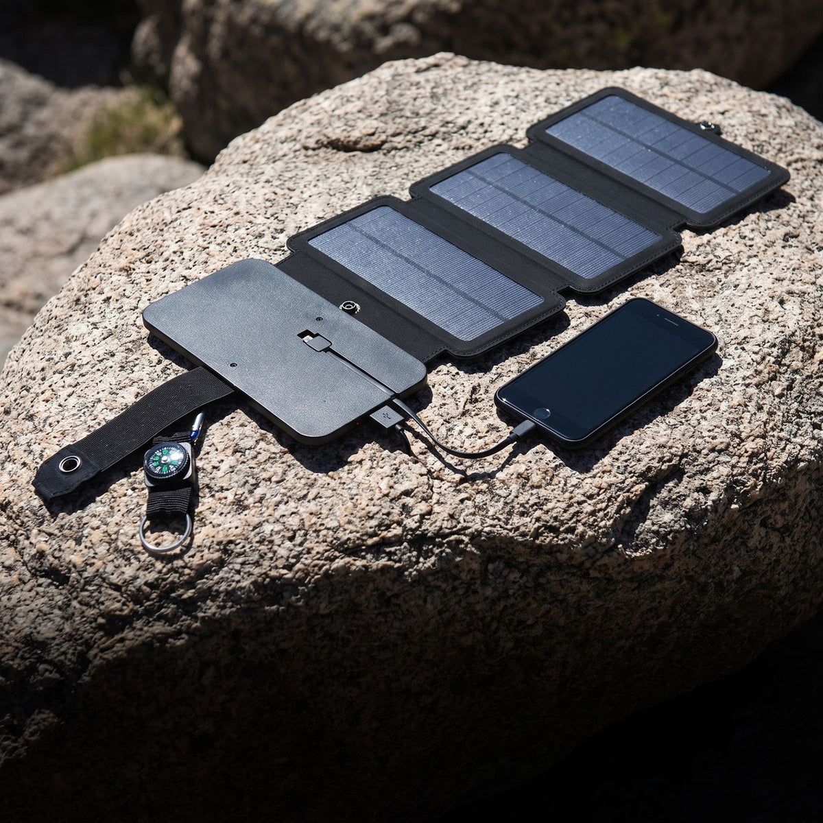 4 Panel Solar Charger unfolded on rock beside a charging phone