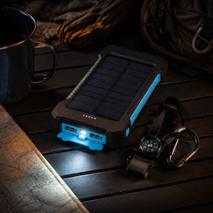 Waterproof Solar Charger on a camp table at night, small LED lit beside a mug
