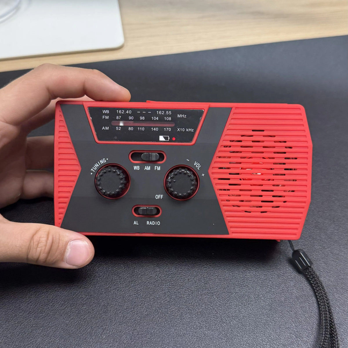 Hand holding the Tacright Emergency Radio, weather band frequencies visible on the dial